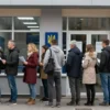 A long queue of people waiting outside a Ukrainian passport office. The people are diverse in age and appearance, holding documents. The building is modern and official-looking. The scene should convey a sense of hope and anticipation.