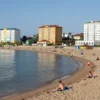 A picturesque view of a Black Sea resort town in the Astrakhan region, featuring several hotels along the coastline. The scene should depict calm blue waters, sandy beaches, and colorful buildings. Include people relaxing on the beach and enjoying the seaside. Focus on the architecture of the hotels and the overall vacation atmosphere.