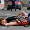 Two school children are lying on the road, surrounded by debris from cars. Emergency vehicles (ambulances, police cars) are present at the scene. The background shows a city street in Volgograd. Focus on the children's expressions of shock and the chaotic aftermath of the accident.