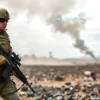 A lone soldier, clad in camouflage, stands amidst a desolate, war-torn landscape. Smoke rises in the background, and the sky is overcast. The soldier has a determined expression, holding a rifle. Focus on the soldier's equipment and the harsh environment.
