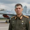 A realistic portrait of a Soviet Hero of the Russian Federation, a military pilot, standing in front of a backdrop depicting a fighter jet and a cloudy sky. The portrait should convey strength, determination, and patriotism.