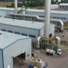 A modern industrial complex in the Southern Urals region, with several factories and warehouses. Workers in hard hats are seen inspecting equipment. The scene should convey economic development and investment.