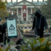 A realistic scene of a graduation ceremony in a park with several graduates wearing caps and gowns, standing together. In the foreground, a shadowy, hooded figure approaches one graduate, holding a smartphone that displays a generic phishing warning icon (no text). The background shows a university building and a banner with a subtle, abstract warning symbol. The atmosphere is tense yet subtle, capturing the threat of scammers targeting new graduates.