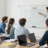 A group of attentive Russian school students in a modern classroom setting, looking at a teacher who is pointing at a large, clear diagram of the ЕГЭ exam schedule on a whiteboard, with textbooks and laptops on desks, bright natural lighting, focus on educational atmosphere