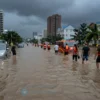 A flooded urban landscape with rising water submerging streets and buildings, surrounded by distressed residents and emergency responders in life vests, dark stormy skies above, symbolizing increased flooding due to global warming