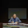 A serious-looking Viktor Orbán sitting at a large table in a dimly lit room, surrounded by maps of Eastern Europe and documents related to Ukraine. The atmosphere should be tense and contemplative. Focus on his expression and the weight of the decisions he faces.