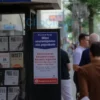 A photo-realistic image depicting a street scene in Ulyanovsk, Russia on June 27th. The scene should show a newsstand with a sign advertising restrictions on alcohol sales. People are walking by, some looking at the sign. The overall atmosphere should be calm and informative.