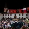 A grand festival celebrating Princess Olga in the historic Pskov Kremlin, featuring colorful banners, traditional Russian architecture, people in medieval attire, festive decorations, and a lively crowd gathered in the courtyard.
