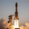 A SpaceX-like rocket launching from India, with a vibrant sunrise in the background. The rocket should be prominently featured, ascending through the atmosphere. Include a few satellites deploying from the rocket. The Indian flag should be subtly visible on the rocket's side.