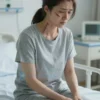 A woman in her late 30s, looking exhausted and distressed, sitting on a hospital bed. She has visible scars from a recent surgery on her face and neck. The room is sterile and brightly lit. Focus on her emotional state and the physical aftermath of the surgery.