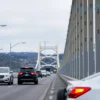 A wide shot of the Crimean Bridge with vehicles moving across it. The sky is overcast, suggesting the aftermath of an event. Focus on the traffic flow and the bridge's structure.