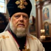 A solemn portrait of Patriarch Kirill of Moscow standing in a dignified pose, wearing traditional Orthodox vestments with a golden cross, against a softly blurred background of a historic Russian cathedral interior with candlelight and icons, conveying moral authority and spiritual gravity