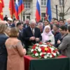 A solemn farewell ceremony for the leader of the housing and communal services department in the Melekessky district. The scene should depict a group of people gathered in a respectful and dignified manner, possibly in a public square or a government building. The leader should be at the center, surrounded by colleagues, friends, and possibly local officials. The atmosphere should convey a sense of respect and gratitude. The setting should include elements like flags, wreaths, and possibly a pod
