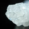 A close-up, highly detailed image of a crystalline structure resembling a sugar crystal, with subtle, shimmering energy fields emanating from within. The crystal is illuminated by a soft, diffused light, highlighting its intricate internal patterns. The background is dark and out of focus, emphasizing the crystal's luminosity.
