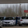 A gas station in Chelyabinsk with long lines of cars waiting to refuel, showing rising fuel prices on digital signs and people discussing costs inside the station