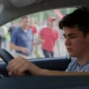 A 17-year-old driver intentionally driving a car through a crowded city center, with pedestrians and vehicles around, showing a sense of urgency or recklessness in the scene