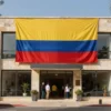 A modern and elegant building with the Colombian flag prominently displayed, situated in Jerusalem. The building should have a welcoming entrance with people entering and exiting, symbolizing the opening of the embassy. The surrounding area should show a mix of urban and cultural elements, reflecting the unique blend of Colombian and Jerusalemite influences.