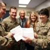 A group of soldiers in military uniforms receiving tax documents and financial assistance from a government official, with their families smiling in the background, symbolizing tax relief and support for veterans and their loved ones