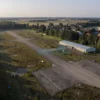Aerial view of rural European Russia at dawn, showing abandoned airports with overgrown runways, empty terminal buildings, and quiet surrounding landscapes with forests and small villages, no aircraft or people present