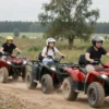 A group of people riding quad bikes on a dirt road in a rural area near Kostroma, Russia. The scene should capture the joy and freedom of the activity, with the riders wearing helmets and appropriate safety gear. The background should include elements of nature such as trees and fields, emphasizing the outdoor setting.