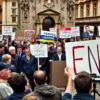A political protest scene in a European capital city with diverse crowd holding signs that read 'Stop Funding Ukraine' and 'End Military Aid', featuring a former government official speaking at a podium, realistic clothing and architecture, muted color palette, no text or symbols on signs, no weapons