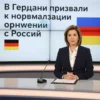 A formal news broadcast scene showing a German news anchor in a studio setting, with a large screen behind them displaying the headline "В Германии призвали к нормализации отношений с Россией" in Russian, alongside German and Russian flags, serious atmosphere, professional lighting, medium shot