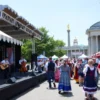 A vibrant festival scene in Ulyanovsk, showcasing traditional Russian music and cultural activities. The image should include a stage with musicians playing traditional instruments, people in traditional Russian attire dancing and celebrating, and various stalls selling traditional crafts and food. The background should feature iconic landmarks of Ulyanovsk, such as the Lenin Memorial Complex, under a clear blue sky.