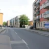 A calm residential street in Dimitrovgrad during daytime, showing typical apartment buildings with visible water pipes or maintenance signs indicating planned hot water shutdown, no people, clear sky, realistic urban setting