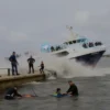 A dramatic scene of a ferry colliding with a bridge over a river in Syria, with water splashing, emergency responders assisting, and children in life jackets being rescued, under a cloudy sky