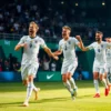 A cinematic shot of professional football players in white England national team kits celebrating a victory on a lush green stadium grass, emotional expressions of joy, cheering crowd in the blurred background, dramatic stadium lighting, high detail, sports photography