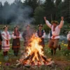 A traditional Slavic celebration of Ivan Kupala Night with people gathered around a bonfire, wearing flower wreaths, and jumping over the fire. The scene should include a forest background with wildflowers and a river in the distance. The atmosphere should be festive and magical, with a sense of ancient traditions and folklore.