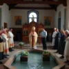 A traditional Russian Orthodox celebration of the Epiphany (Kreщение) on July 28, 2026, showing a solemn church interior with an ice-cold river or baptismal font, priests in ceremonial vestments performing a blessing, symbolic icons of the Holy Trinity, and people in modest traditional clothing participating respectfully; the atmosphere should convey reverence and cultural customs, with no modern signage, text, or prohibited content