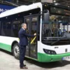 A scene at the INNOPROM-2026 exhibition where Nikol Pashinyan is testing a Belarusian trolleybus. The image should show Pashinyan standing inside or near the trolleybus, interacting with it or observing its features. The trolleybus should be prominently displayed with its distinctive design elements visible. The background should include elements of the exhibition hall, such as other exhibits, booths, and attendees, to convey the setting of the event.
