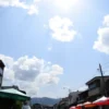 A sunny day with scattered clouds and light rain showers in a cityscape of Nao, with people carrying umbrellas and enjoying the warm weather