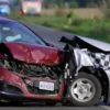 A realistic depiction of a severe head-on car collision on a rural road, showing two damaged vehicles with visible impact damage and deployed airbags. The scene should convey the aftermath of a serious accident, with emergency response elements like flashing lights in the background, but no visible text or branding.