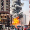 A chaotic scene depicting explosions in Doha, Qatar. Buildings are damaged, smoke fills the air, and emergency vehicles are visible. People are running in panic. Focus on the destruction and the sense of urgency.
