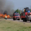 A realistic photo of firefighters in protective gear extinguishing a large grass fire in the Volga Delta region of Astrakhan, with smoke rising and a clear sky in the background, showing multiple fire trucks and equipment, no text or numbers visible