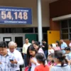 A modern school building with a digital sign displaying the number of applications received through government services. The scene should include a diverse group of people, including parents and children, gathered outside the school, some using smartphones or tablets. The atmosphere should be lively and positive, with a focus on the convenience of digital services.