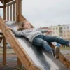 A young girl falling from a decaying wooden playground slide in Blagoveshchensk, Russia, with visible rot and broken planks, overcast sky, urban residential background, realistic details, no text or symbols