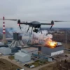 Aerial view of a Ukrainian UAV (drone) flying over a power plant (ТЭК) in Ulyanovsk Oblast, with smoke or damage visible on the facility, showing a military or combat scenario. Include details like the drone in the sky, the power plant structure, and possible explosions or fire effects in the background.