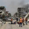 A devastated Venezuelan cityscape after a massive earthquake, with crumbled buildings, collapsed roads, and emergency responders assisting survivors amid rubble. Smoke rises in the background, and a somber sky reflects the ongoing tragedy.