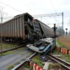 A freight train derails and collides with a discarded car on a railway crossing in the Volgograd region. The scene is set during a cloudy day. Focus on the wreckage and the surrounding environment.