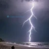 A dramatic scene of a powerful lightning strike hitting the United States, showing a beach with a person being struck by lightning while relaxing on the sand, realistic weather effects, dark stormy sky, bright lightning bolt illuminating the scene, no text or symbols on the image