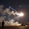 Four drones being shot down over Moscow, with smoke trails and explosions in the night sky, city skyline in the background, military personnel observing from a distance, dramatic lighting