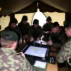 A military signal tent in Kyiv, Ukraine, with soldiers in uniform gathered around a communication device, showing a map and tactical discussion. Include elements like a flag, military gear, and a focused atmosphere.