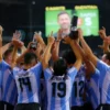 A dynamic sports scene showing an Argentine soccer team celebrating a hard-fought victory over Cabo Verde, with players in Argentina's sky-blue and white jerseys raising arms and trophies, stadium lights, crowd cheering, and the scoreboard displaying a close final score, photorealistic-1