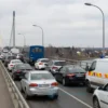 A view of the Crimean Bridge with vehicles stopped and blocked on the bridge, overcast sky, and emergency vehicles nearby, showing a temporary closure situation