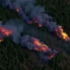 A realistic aerial view of Yakutia showing multiple forest fire hotspots with visible flames and smoke plumes over dense taiga forest, no text or symbols
