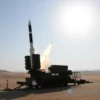 A high-quality image of a Chinese ballistic missile launch test. The scene should depict the missile being launched from a mobile launch platform in a desert or military testing area. The missile should be in the early stages of ascent, with a trail of smoke and flames visible. The background should include military personnel observing the launch from a safe distance, and the sky should be clear with a bright sun. The image should convey a sense of technological advancement and military capabili