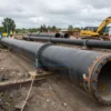 A heavily worn and damaged 60-meter pipeline being replaced in Voronezh, with construction workers, machinery, and new pipeline sections visible in an industrial setting